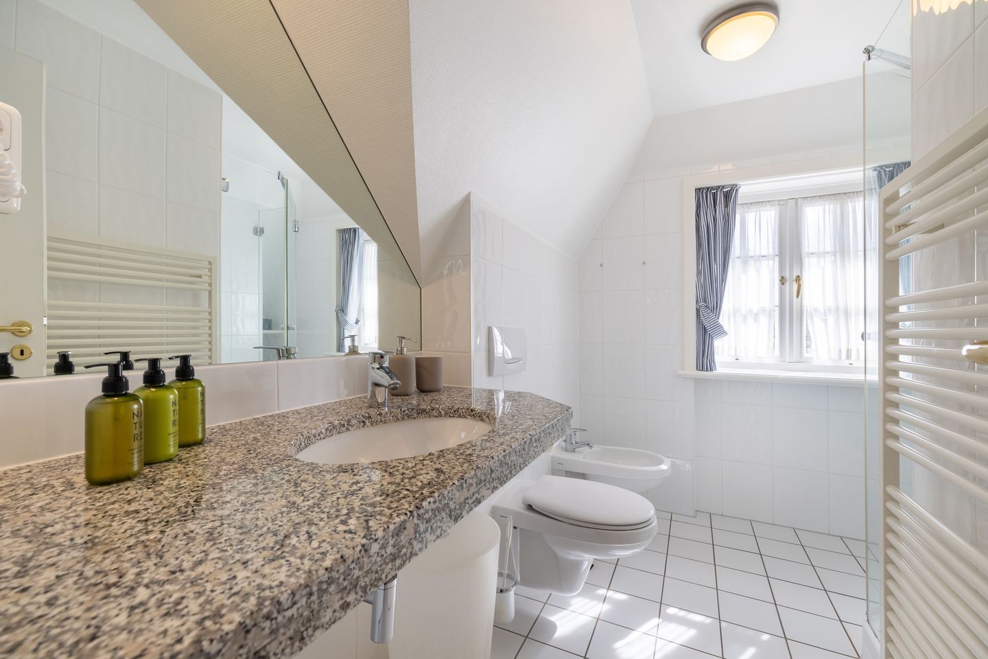 Un baño moderno con dos lavamanos, una ducha y un inodoro. Hay tres botellas de loción en la encimera.