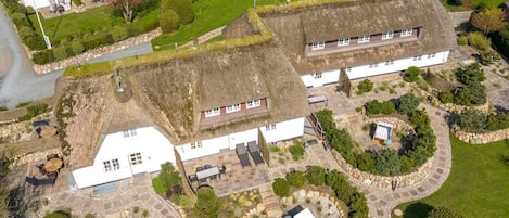 A large estate with multiple buildings, including a main house with a thatched roof, several smaller outbuildings, and a well-maintained garden with stone pathways and various plants.
