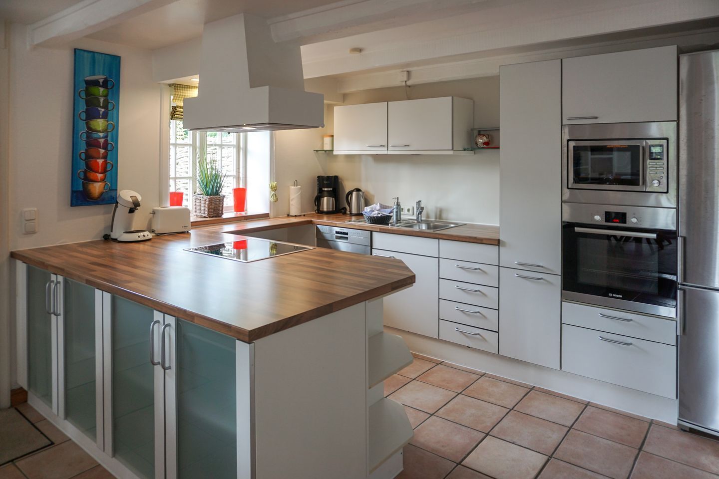 A modern kitchen with a central island, white cabinetry, stainless steel appliances, and a window with natural light.