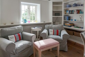 A living room with two grey armchairs, a small round table, and a bookshelf filled with books and decorative items.