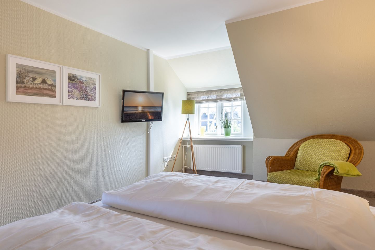 A hotel room with a bed, a chair, a TV, and two framed pictures on the wall.