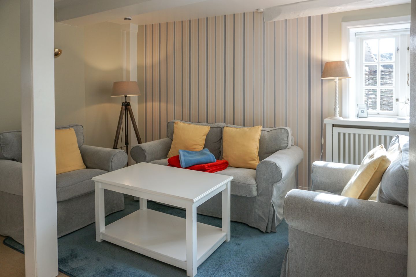 A living room with two grey sofas, a white coffee table, and striped wallpaper.