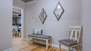 Ein Zimmer mit einer hölzernen Bank und einem Stuhl, einem an der Wand befestigten Spiegel und einer Tür zu einem Essbereich.