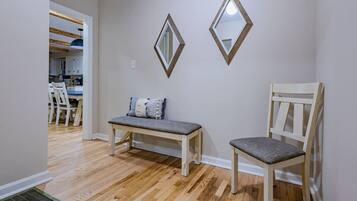 Une pièce comprenant un banc en bois et une chaise, un miroir fixé au mur, et une porte donnant sur un coin repas.
