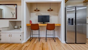 Eine kleine Küche mit integriertem Kühlschrank, einer Holz Arbeitsplatte, zwei Barhocker, einem an der Wand montierten Fernseher und einem Spiegel.