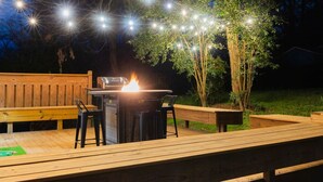 Eine Terrasse im Freien mit Feuerstelle, Lichterketten und Holzbanken.