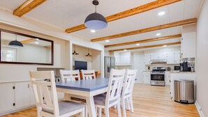 Eine geräumige Küche mit weißen Schränken, ein Essbereich mit blauem Tisch und weißen Stühlen sowie Holzbalken an der Decke.