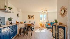 A modern kitchen with blue cabinets, a dining area with a blue sofa, and a large window providing natural light.