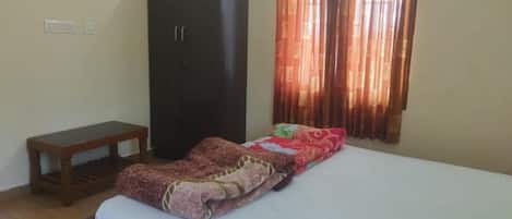 A bedroom with a bed, a wardrobe, a bench, and a window with curtains.