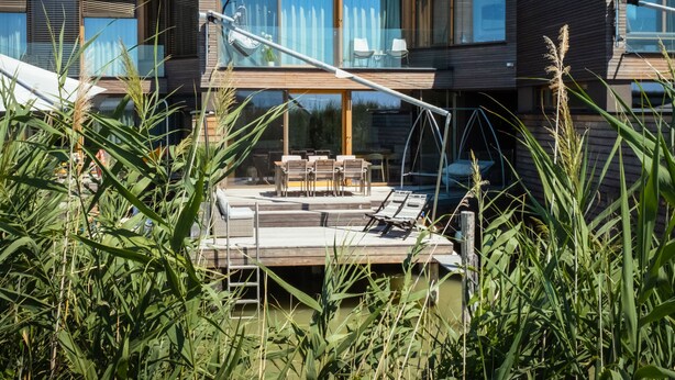 Ein modernes, zweistöckiges Haus mit Terrasse, Gartenmöbeln und einer Schaukel.