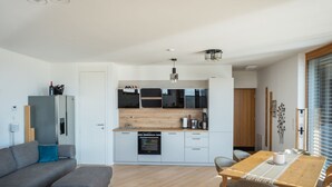 Eine moderne Küche mit Einbauofen, ein Essbereich mit Holztisch und -stühlen sowie ein graues Sofa im Wohnbereich.