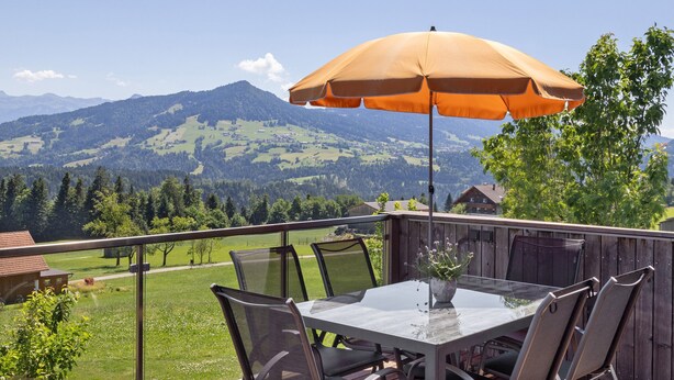Een tafel met stoelen en een parasol op een balkon met uitzicht op een berg.