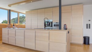 Een moderne keuken met een groot eiland, inbouwapparatuur en grote ramen met uitzicht op de omgeving.