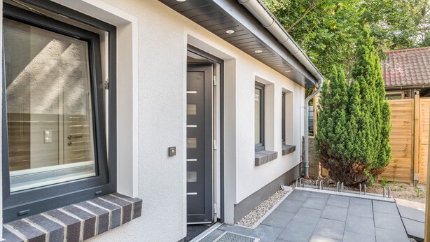 Ein modernes Haus mit einem großen Fenster, einer Tür und einem kleinen Baum im Garten.