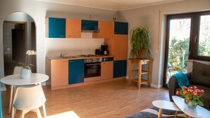 A modern kitchen with wooden cabinets, a stove, and a sink. There is a dining area with a table and chairs, and a plant on a small table. - Apartment 'Ferienwohnung Maintalblick' with Private Terrace, Private Garden and Wi-Fi (Eltmann)