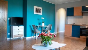 A modern kitchen with a stove, oven, and blue cabinets. There is a dining area with a white table and chairs, and a TV on a white cabinet. - Apartment 'Ferienwohnung Maintalblick' with Private Terrace, Private Garden and Wi-Fi (Eltmann)