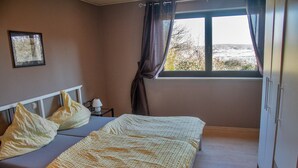 A bedroom with a bed, pillows, a nightstand, a window with curtains, and a picture on the wall. - Apartment 'Ferienwohnung Maintalblick' with Private Terrace, Private Garden and Wi-Fi (Eltmann)