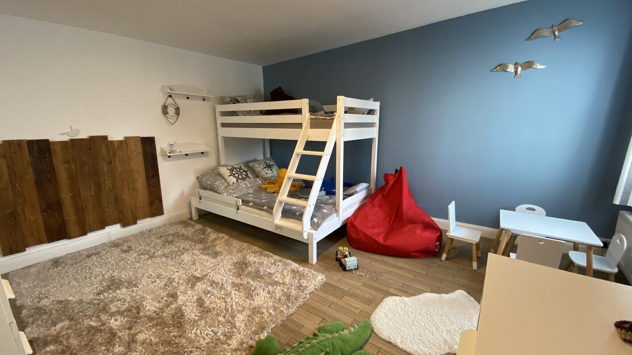 A bunk bed with a ladder, a desk, a chair, a red bean bag, and a small table.