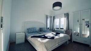 Un dormitorio ordenado con cama, mesitas de noche, un armario y una ventana con cortinas.