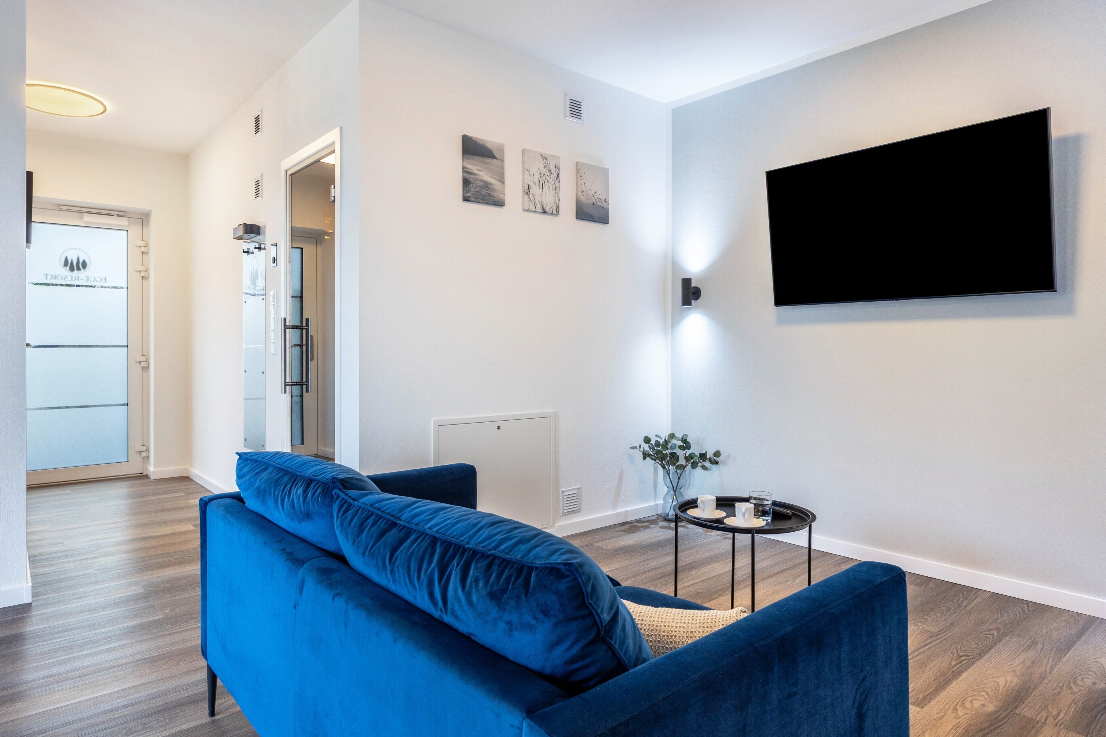 Una sala de estar moderna con un sofá azul, un televisor de pantalla plana y una mesita con un florero.