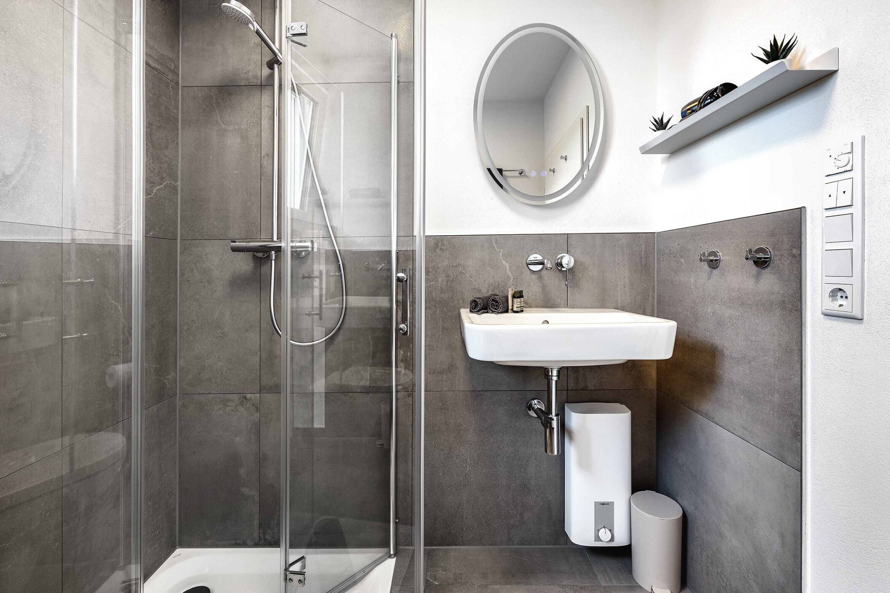 Une salle de bain moderne avec une douche à parois de verre, un lavabo blanc et un miroir rond.