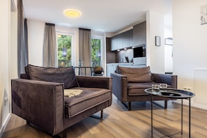 A modern living room with two brown leather sofas, a small round table with glasses, and a kitchen in the background.