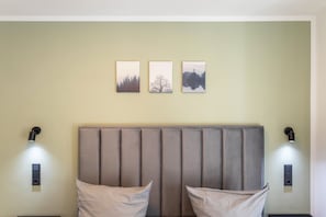 A room with a padded headboard, two bedside lamps, and three framed pictures on the wall.