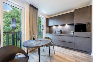 A modern kitchen with dark cabinets, a built-in oven, and a dining area with a round table and chairs.