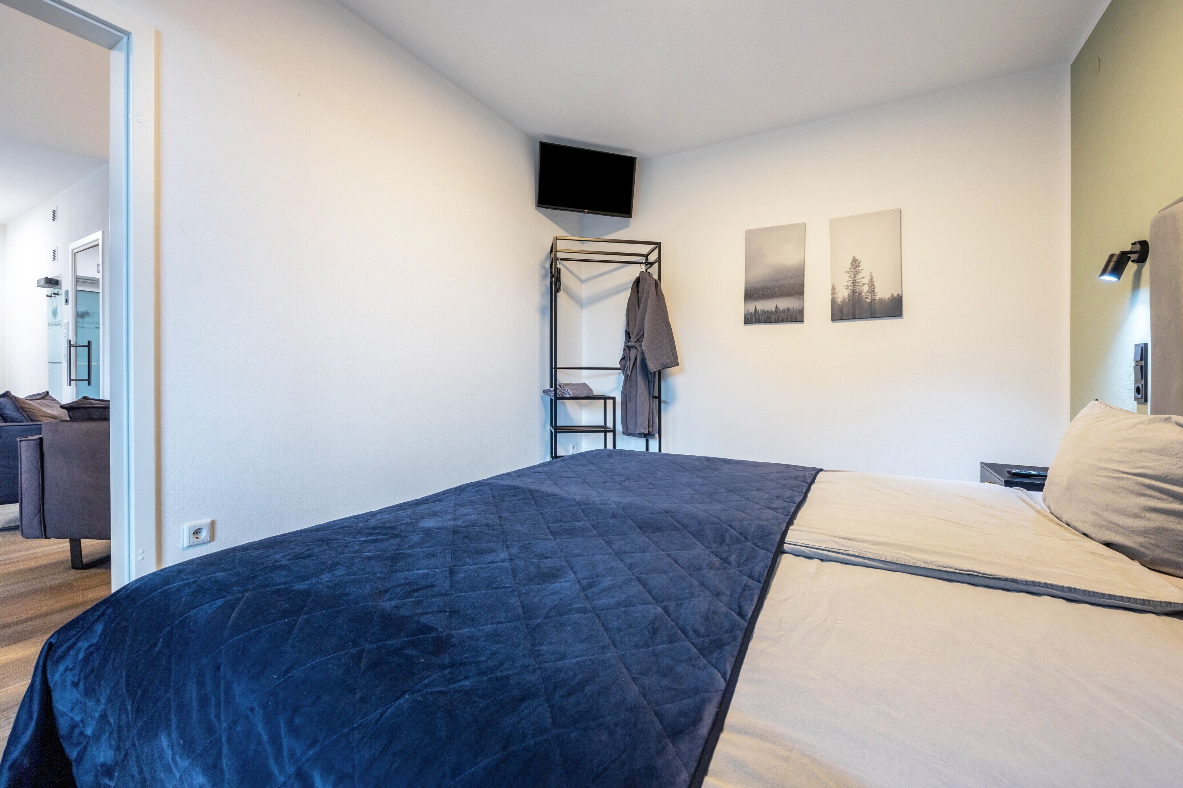 Ein Schlafzimmer mit einem Bett, einem an der Wand montierten Fernseher und einem Kleiderständer.