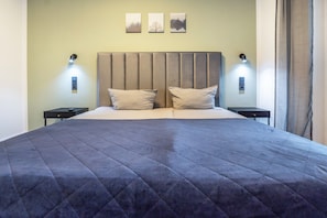 A bed with a quilted cover, two bedside tables, a wall-mounted light fixture, and three framed pictures on the wall.