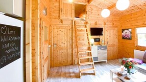 A wooden cabin interior with a wooden staircase, a sofa, a table with flowers, and a chalkboard with text. - Holiday Home 'Ferienhaus 5 Familie Täubert' with Private Terrace, Private Garden and Wi-Fi (Boxberg/Oberlausitz)