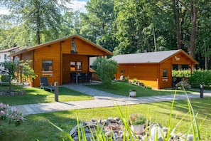 Una cabaña de madera con porche, comedor y un pequeño jardín.