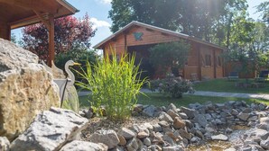 A wooden cabin with a stone structure in the foreground, surrounded by a well-maintained garden and a small stream. - Holiday Home 'Ferienhaus 5 Familie Täubert' with Private Terrace, Private Garden and Wi-Fi (Boxberg/Oberlausitz)
