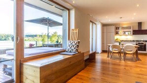 A modern kitchen with wooden cabinets, a dining table with chairs, and a large window overlooking a scenic view. - Apartment "Seen-Sucht" with Lake View, Shared Garden & Wi-Fi (Bad Endorf)