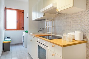 Une cuisine compacte dotée d’un plan de travail en bois, d’un four encastré et d’une fenêtre avec des volets en bois.
