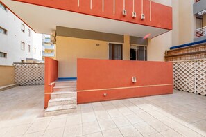 Un immeuble résidentiel à la façade rouge, avec un escalier menant à l’entrée et une terrasse carrelée.