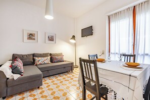 Un salon comprenant un canapé, une table à manger avec des chaises, un téléviseur fixé au mur et un sol à motifs.