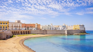 A coastal town with a curved waterfront, historic buildings, and a prominent fortification. - Caddipulina Apartment in Gallipoli 200m From Sea (Gallipoli)