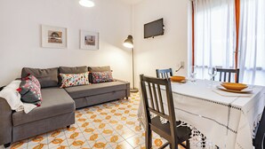 A living room with a sofa, a dining table with chairs, a TV mounted on the wall, and a patterned floor. - Caddipulina Apartment in Gallipoli 200m From Sea (Gallipoli)