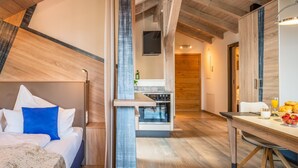 A modern hotel room with a bed, a dining table with breakfast, a kitchen area, and a TV mounted on the wall. - Apartment "Ambiente" with Lake View, Shared Garden & Wi-Fi (Bad Endorf)