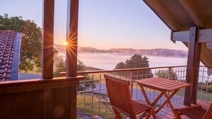 A wooden deck with a table and chairs overlooking a lake at sunrise. - Apartment "Ambiente" with Lake View, Shared Garden & Wi-Fi (Bad Endorf)
