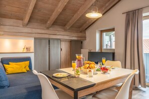 A dining area with a table set for breakfast, a sofa with yellow cushions, and a wooden ceiling. - Apartment "Ambiente" with Lake View, Shared Garden & Wi-Fi (Bad Endorf)