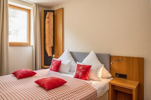 A hotel room with a bed, pillows, a nightstand, a wooden headboard, a window, and curtains.