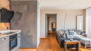 A modern kitchen with a built-in oven and a flat-screen TV. A hallway leads to a living area with a sofa and a coffee table. - Apartment "Wellvital" with Private Terrace & Wi-Fi (Bad Endorf)