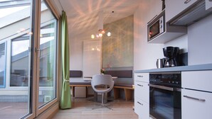 Moderni keittiö, jossa on sisäänrakennettu uuni, kahvinkeitin sekä ruokailutila, jossa on tuoli ja pöytä.