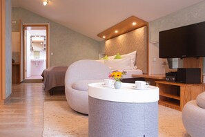 Une chambre d’hôtel moderne équipée d’un lit, d’une télévision, d’une table basse ronde agrémentée d’un vase, et d’un coin salon.
