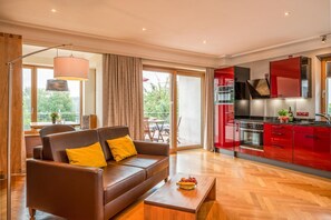 Een moderne woonkamer met een bank, salontafel, en een rode keuken met kasten en apparatuur.