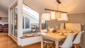 Un espace de salle à manger moderne avec une grande fenêtre, une table en bois, des chaises blanches et un luminaire suspendu.