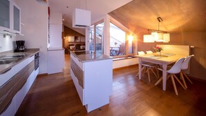 Une cuisine moderne dotée d’un îlot central, d’un coin repas avec une table et des chaises, et offrant une vue sur l’extérieur.