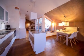 A modern kitchen with a central island, a dining area with a table and chairs, and a view of the outdoors. - Apartment "Loft 7" with Lake View, Shared Garden & Wi-Fi (Bad Endorf)